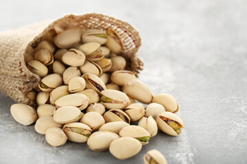 Tasty pistachios in sack on grey background