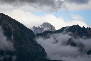 Dramatic dolomite rock between clouds with green forest below