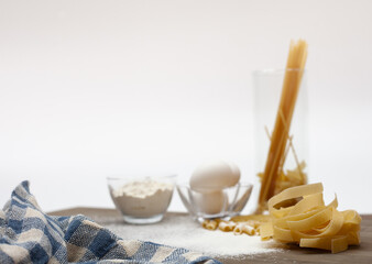 Pasta dough with eggs and cup of flour on white background with blur on the cloth in front.