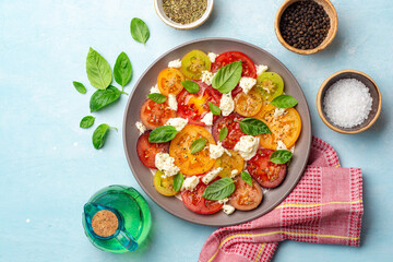 Italian caprese salad with varicolored tomatoes, mozzarella cheese, basil leaves, spices and olive oil in plate on concrete background