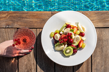 refreshing cocktail and fruits and berries plate near swimming pool in hotel