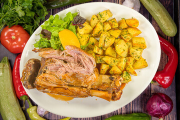 Tasty pork knuckle with oven potatoes in a dish on the table.