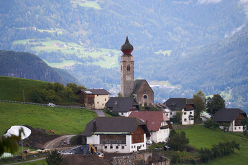Panoramic view of idyllic mountain scenery in the Dolomites with a little village with a beautiful church tower, 2020