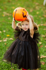 A cute little girl in a witch costume walks in the street with a candy in the shape of a pumpkin. The concept of Halloween