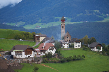 Panoramic view of idyllic mountain scenery in the Dolomites with a little village with a beautiful church tower, 2020