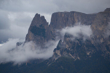 Dramatic dolomite rock between clouds with green forest below
