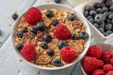 Granola with blueberries and raspberries in white bowl on dark white desk.