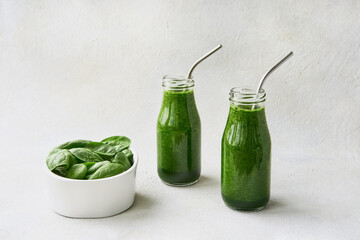 Green spinach smoothie in small bottles and spinach leaves in bowl on white concrete background. Copy space. Healthy lifestyle concept