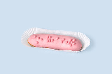 Bright Eclair in pink glaze in wrapping paper, sprinkled with colorful pink jelly beans, balls. Isolated on a blue background.