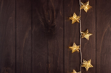 Fashion shimmer festive background -  golden glowing stars on dark brown wood board, border, top view.