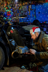 Fototapeta na wymiar A man in a santa claus hat repairs a motorcycle in the garage on New Year's Eve.