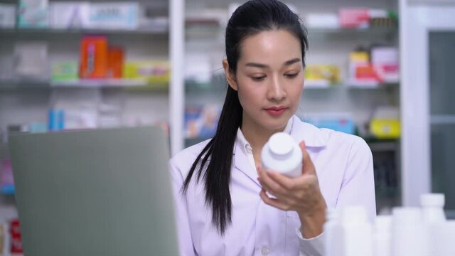 Woman pharmacists using laptop computer devise to type in the information from a pill container is holding