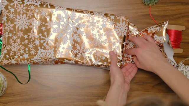 Step-by-step instructions for gift packaging. Shiny gold-colored paper with snowflakes. Step 3. Tuck the paper on both sides.