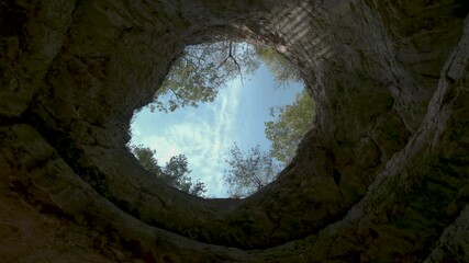 cloudy sky through opening gap in cave ceiling. Camera look vertical up, pan move. - Powered by Adobe