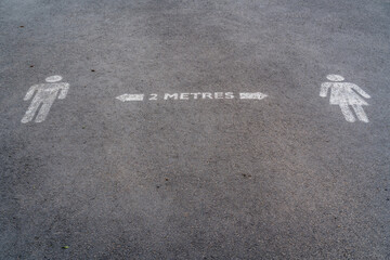 Social distancing road painted sign recommending staying 2 metres apart