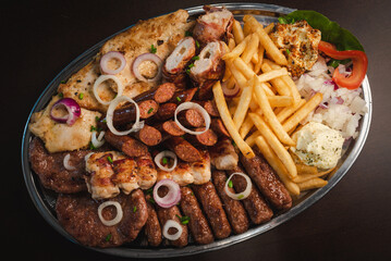 several types of roasted meat served on an oval, Serbian dish 