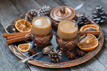 Fototapeta na wymiar Copper cups of hot coffee with cream, with cinnamon, anise on a copper tray and a wooden background.