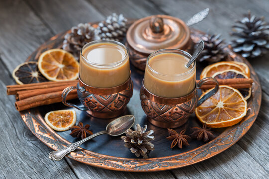 Copper cups of hot coffee with cream, with cinnamon, anise on a copper tray and a wooden background. © Arina B