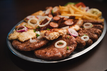 several types of roasted meat served on an oval, Serbian dish 
