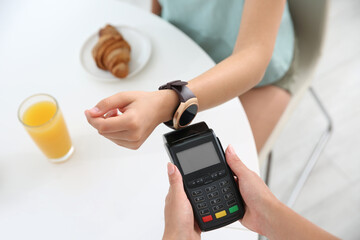 Woman using smart watch for contactless payment via terminal in cafe, closeup