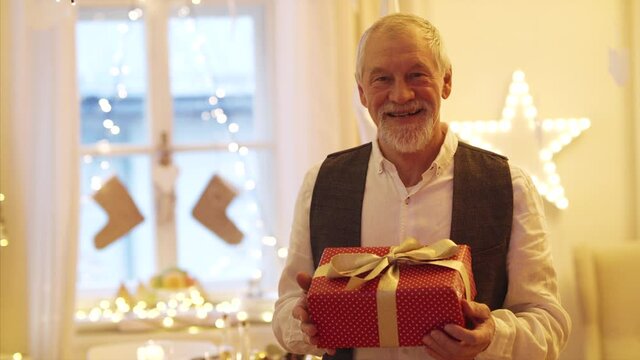 Front view of happy senior man indoors holding present at Christmas.