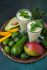 Two glasses of fruit smoothie made from mango, avocado, feijoa and cream on a tray