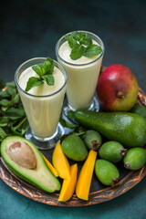 Two glasses of fruit smoothie made from mango, avocado, feijoa and cream on a tray