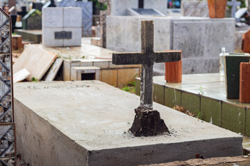 Fototapeta na wymiar Cruz em um túmulo de cimento com detalhes de outros túmulos ao fundo.