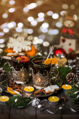 Two glasses of mulled wine in cup holders, with cinnamon and anise on a wooden background with fir branches and candles. Winter Christmas still life, beautiful bokeh, postcard in vintage style.