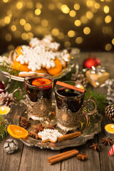 Fototapeta na wymiar Two glasses of mulled wine in cup holders, with cinnamon and anise on a wooden background with fir branches and candles. Winter Christmas still life, beautiful bokeh, postcard in vintage style.