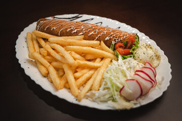 fried roll of meat with cheese with french fries and salad and onion on a plate, Serbian dish 