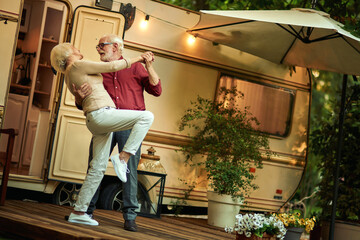 Cheerful married couple enjoying dance outdoors near their motorhome