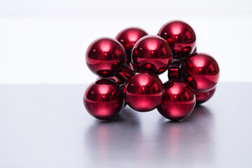 A bunch of red ornaments on a metallic looking reflective surface with a white background