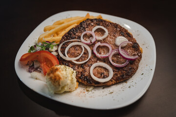 baked barbecue with french fries and salad and onion on a plate, Serbian dish 