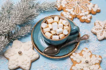 Obraz na płótnie Canvas Cup of coffee with marshmallows, gingerbread cookies in the shape of snowflakes on a blue snowy background. New year idea, concept