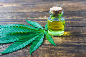 Hemp oil in a glass jar on a hemp leaf stands on a wooden background. Alternative medicine. Hemp oil for cooking. Copy space