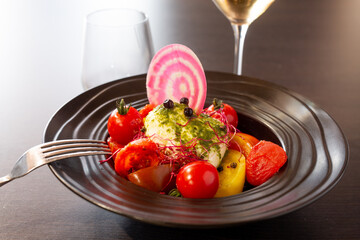 Black plate with fish and tomatoes at a restaurant
