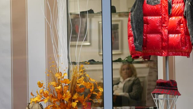 An autumn season warm jacket hangs in a shop window. Pumpkins and other paraphernalia for Halloween. Showcase decoration to attract buyers. Product advertising. Glass windows. Ukraine, Dnipro