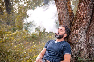 Bearded vaper smoking an electronic cigarette outdoorr. Smoking cessation tobacco.