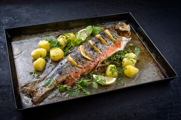 Traditional smoked and roasted char with boiled potatoes and lemon slices offered as close-up on a...