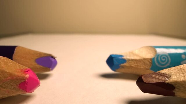 Camera moves above rows of colored pencils. Wooden pencils lie opposite each other in a row. White background. Super macro shot.