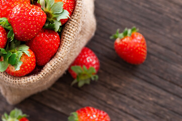 Fresh ripe harvested strawberries in burlap sack on wooden table, Garden summer fruit, strawberry, copy space ( Fragaria )