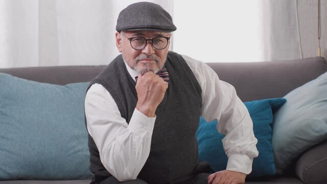 adulto mayor bien parecido con sombrero y anteojos afirmando sentado en una habitaci&oacute;n de casa feliz y tranquilo