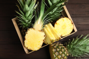 Tasty cut pineapples in crate on wooden table, flat lay