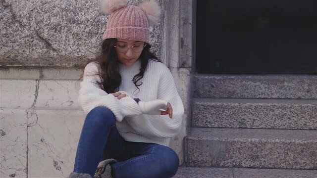 ni&ntilde;a bonita,alegre vestida con ropa de invierno sentada tom&aacute;ndose fotos y mandando mensajes en el celular al aire libre