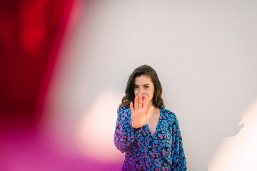 Young woman showing stop sign while standing against wall