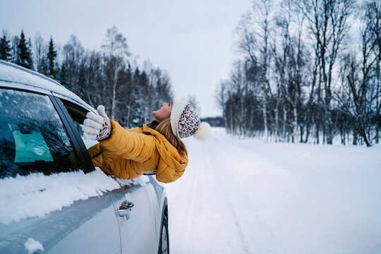 Carefree woman with arms outstretched peeking through car window during winter
