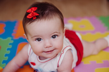 Close-up of cute smiling baby girl lying on puzzle playmat at home