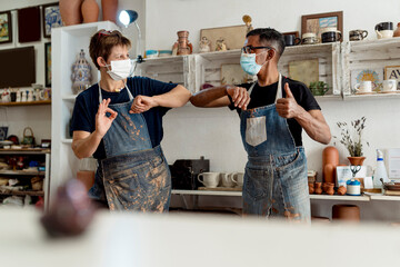 Coworkers wearing masks giving elbow bump while standing in workshop