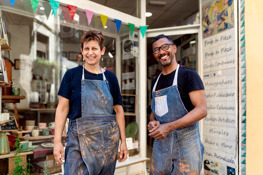Smiling coworkers wearing aprons standing outside ceramic shop - Powered by Adobe